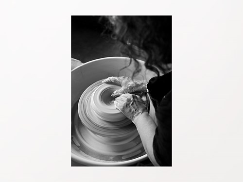 Fotografia en blanc i negre, pla escorç d'una noia modelant amb les mans una peça de ceràmica amb un torn que gira a tota velocitat