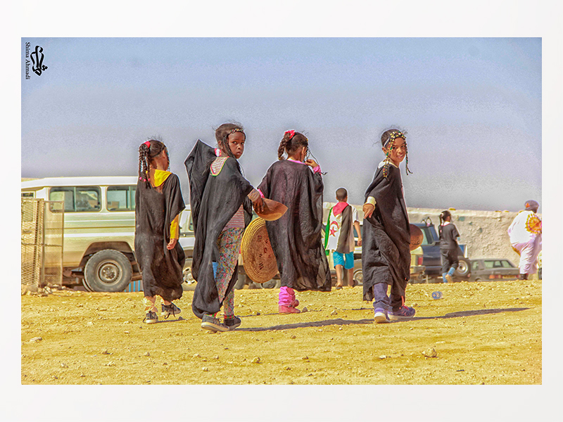 grup de 4 nenes saharauis caminant d'esquenes i 2 miren a càmera, al desert de dia